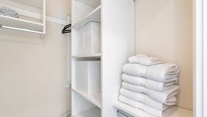 A white closet with shelves, a hanging rod, and a stack of folded towels.