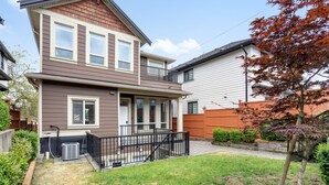 A two-story house with a front porch, a small backyard, and a wooden fence.