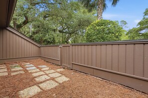 A covered outdoor area with a wooden deck, surrounded by a brown fence, and trees in the background.