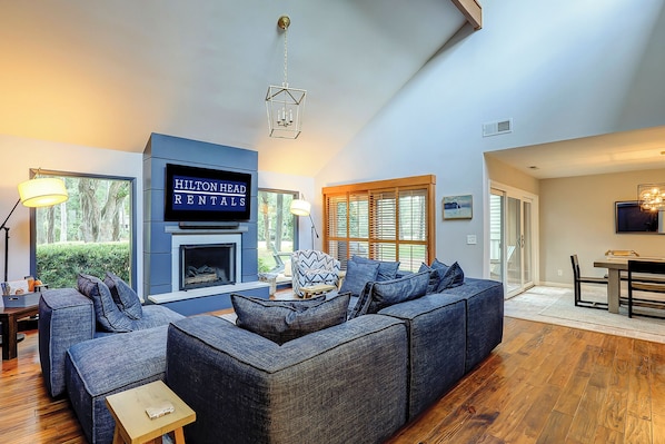 A modern living room with a large sectional sofa, a fireplace, and a television displaying 'Hilton Head Rentals'.