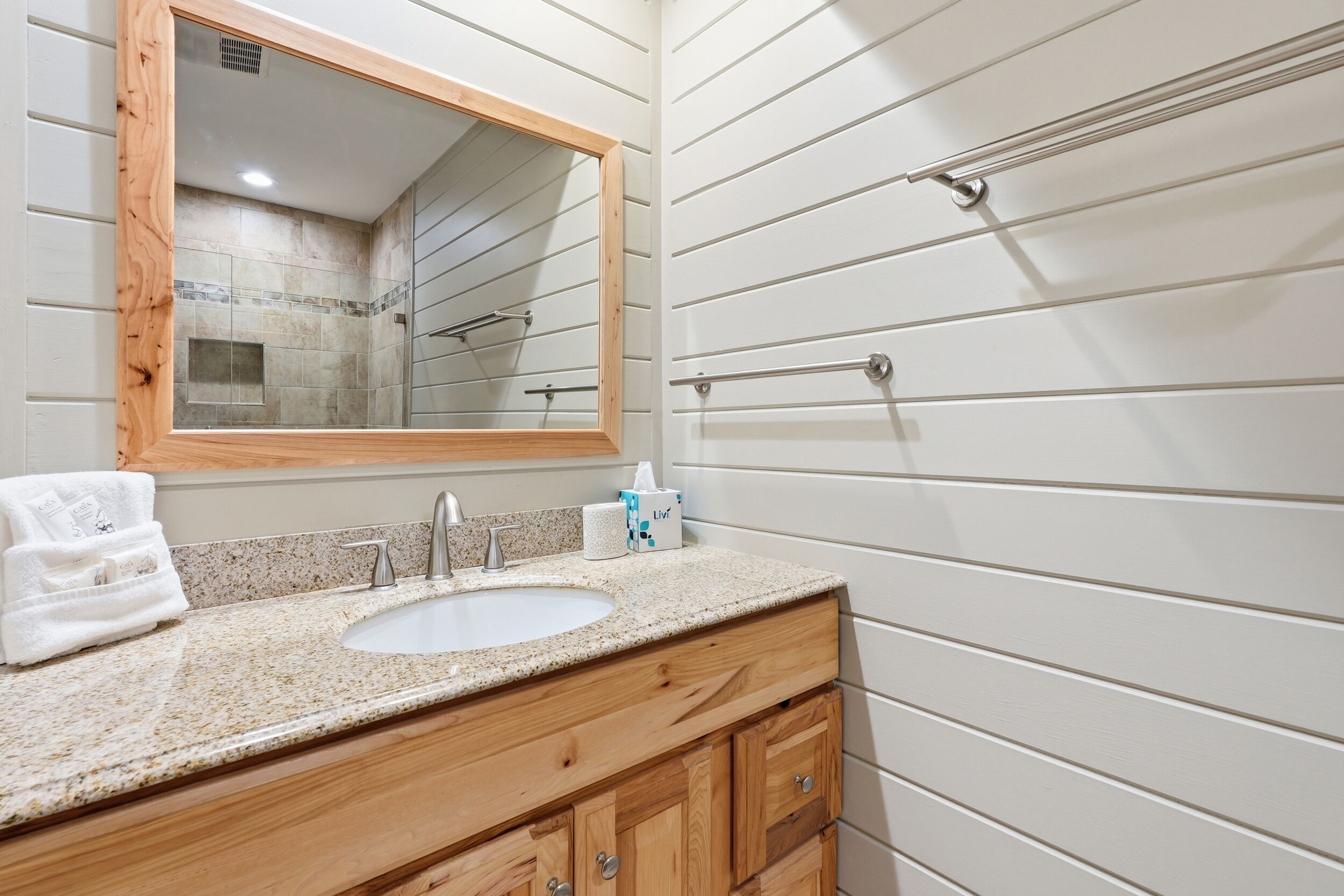A bathroom with a wooden vanity, a sink, a mirror, and a towel rack.