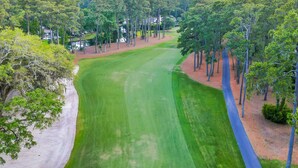Un campo de golf con un camino despejado, rodeado de árboles y algunos edificios.
