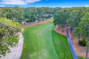 Un campo de golf con un camino despejado, rodeado de árboles y algunos edificios.