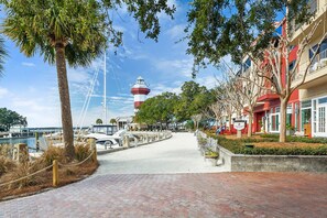 A waterfront promenade with a lighthouse, palm trees, and a row of buildings with balconies.