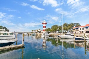 A marina with boats docked, a lighthouse in the background, and buildings with red roofs.