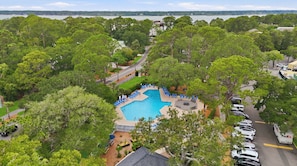A swimming pool surrounded by trees, with a view of a body of water and buildings in the distance.