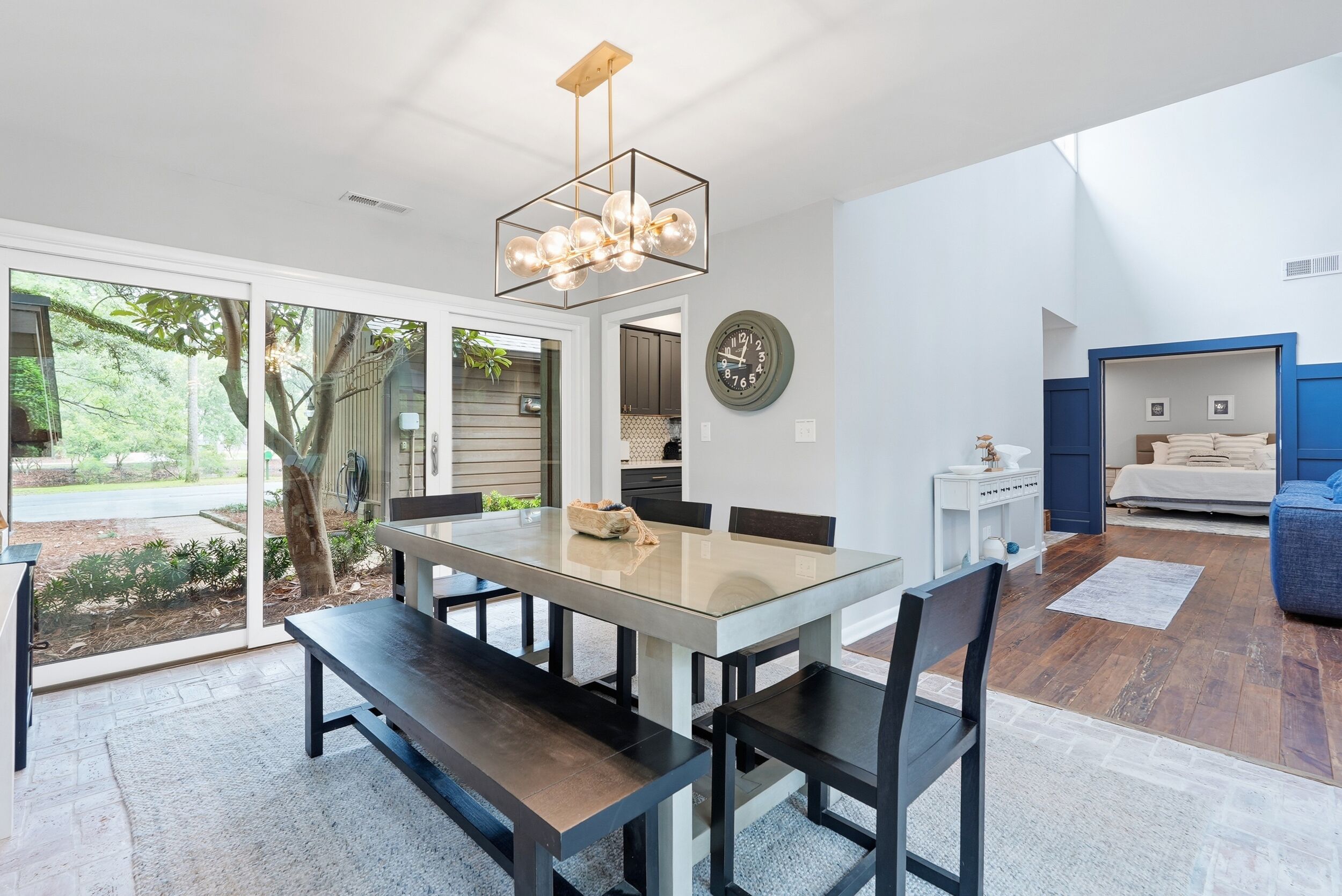 A modern dining area with a glass table, dark chairs, and a chandelier.