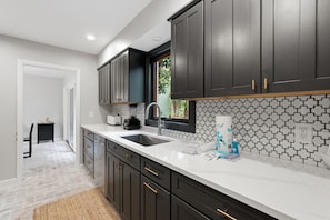 A modern kitchen with dark cabinets, a white countertop, and a window with a view of greenery.