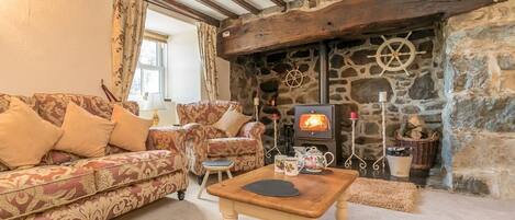 A cozy living room with a stone fireplace, wooden beams, a sofa, and a table.