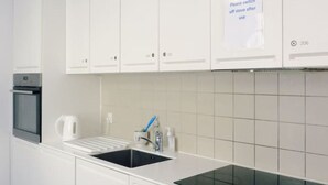 A modern kitchen with white cabinets, a black stovetop, and a sink. There is a sign instructing to switch off the stove after use. - Close to nørreport 206 (København)
