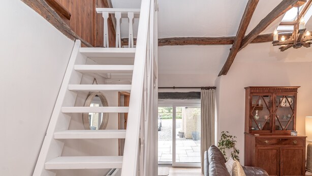 A staircase leading to a second floor, a wooden cabinet, and a leather sofa in a well-lit room with a view outside. - A Cosy Farm Retreat for Two | Muriau-Bach (Criccieth)
