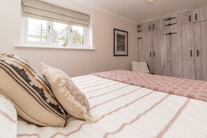 A bedroom with a bed, a window with curtains, a wardrobe, and a framed picture on the wall.