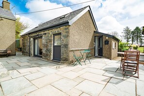 A stone building with a tiled patio, a wooden table, and a chair.