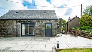 A stone building with a dark roof, a door, and a window. - A Cosy Farm Retreat for Two | Muriau-Bach (Criccieth)