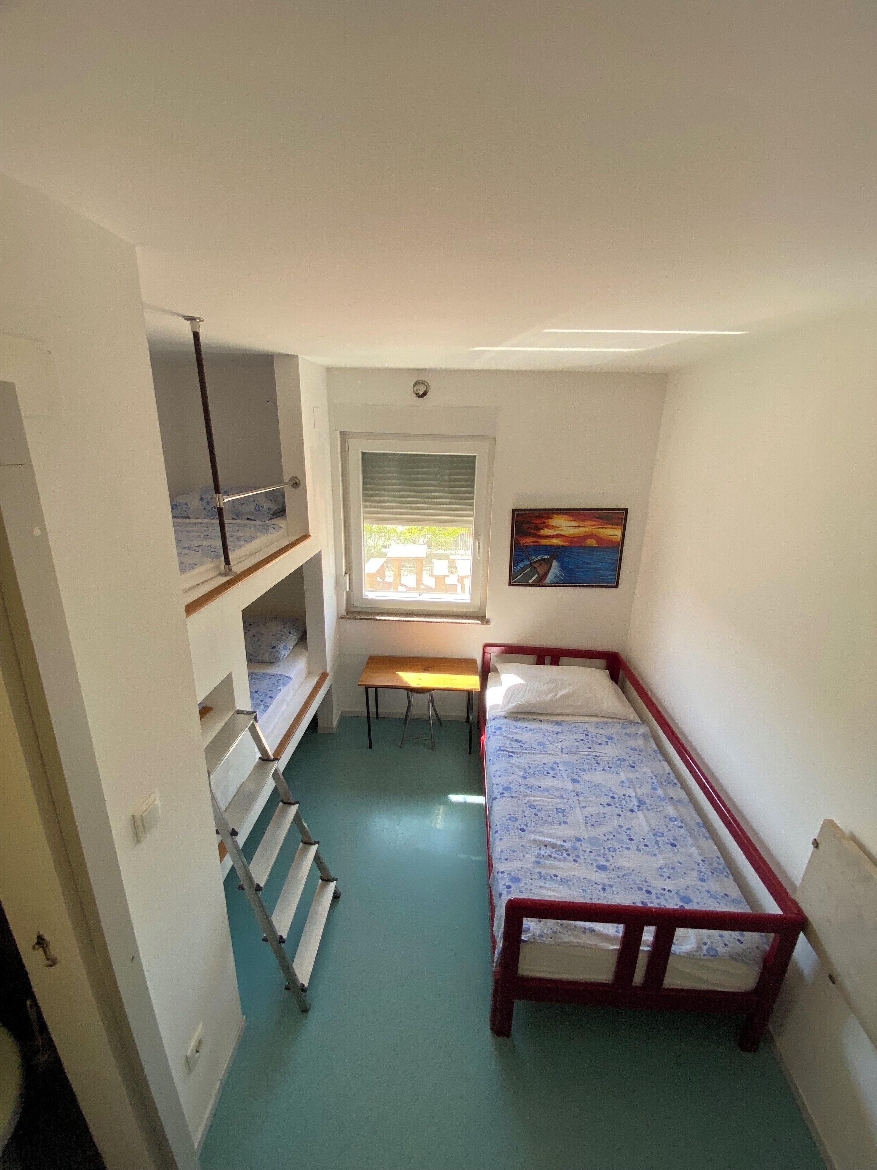 A dormitory room with bunk beds, a desk, and a window with blinds.