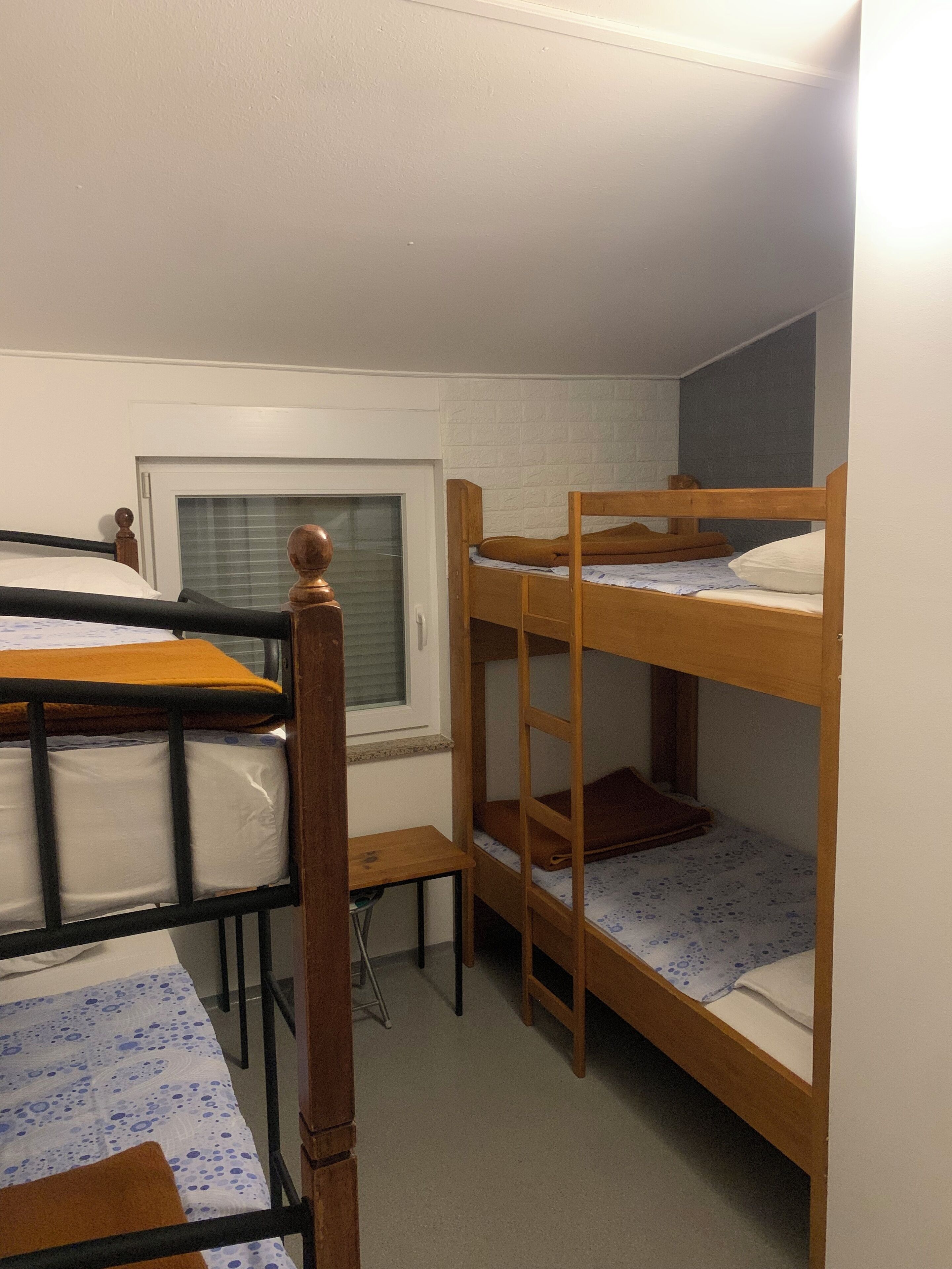 Une chambre de dortoir avec deux lits superposés, une fenêtre avec des stores, un petit bureau et une chaise.