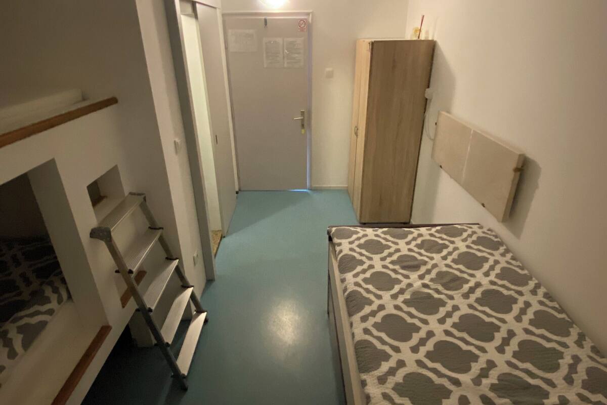 A narrow hallway with a bed on the right, a wardrobe, and a door at the end.