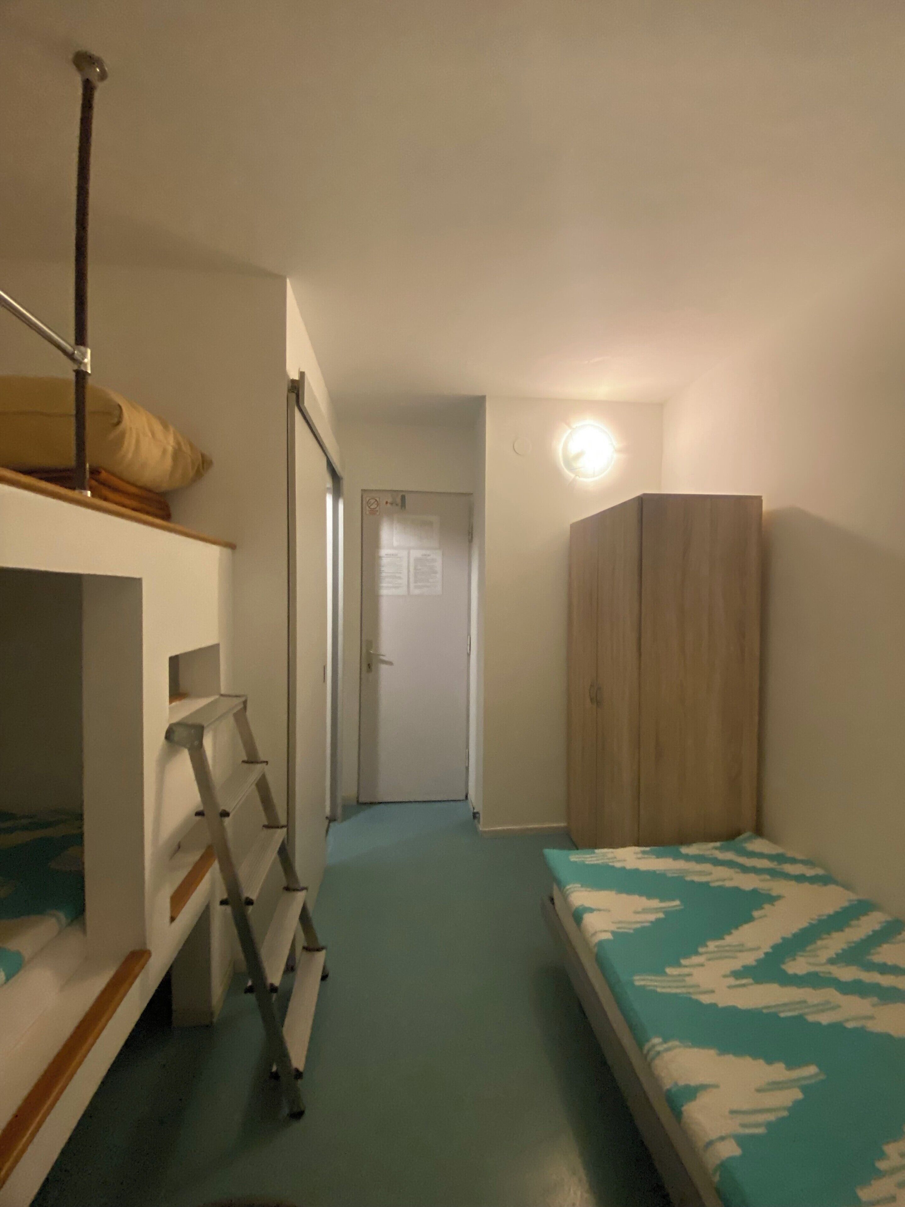 A compact room with bunk beds, a wardrobe, and a door leading to another room.