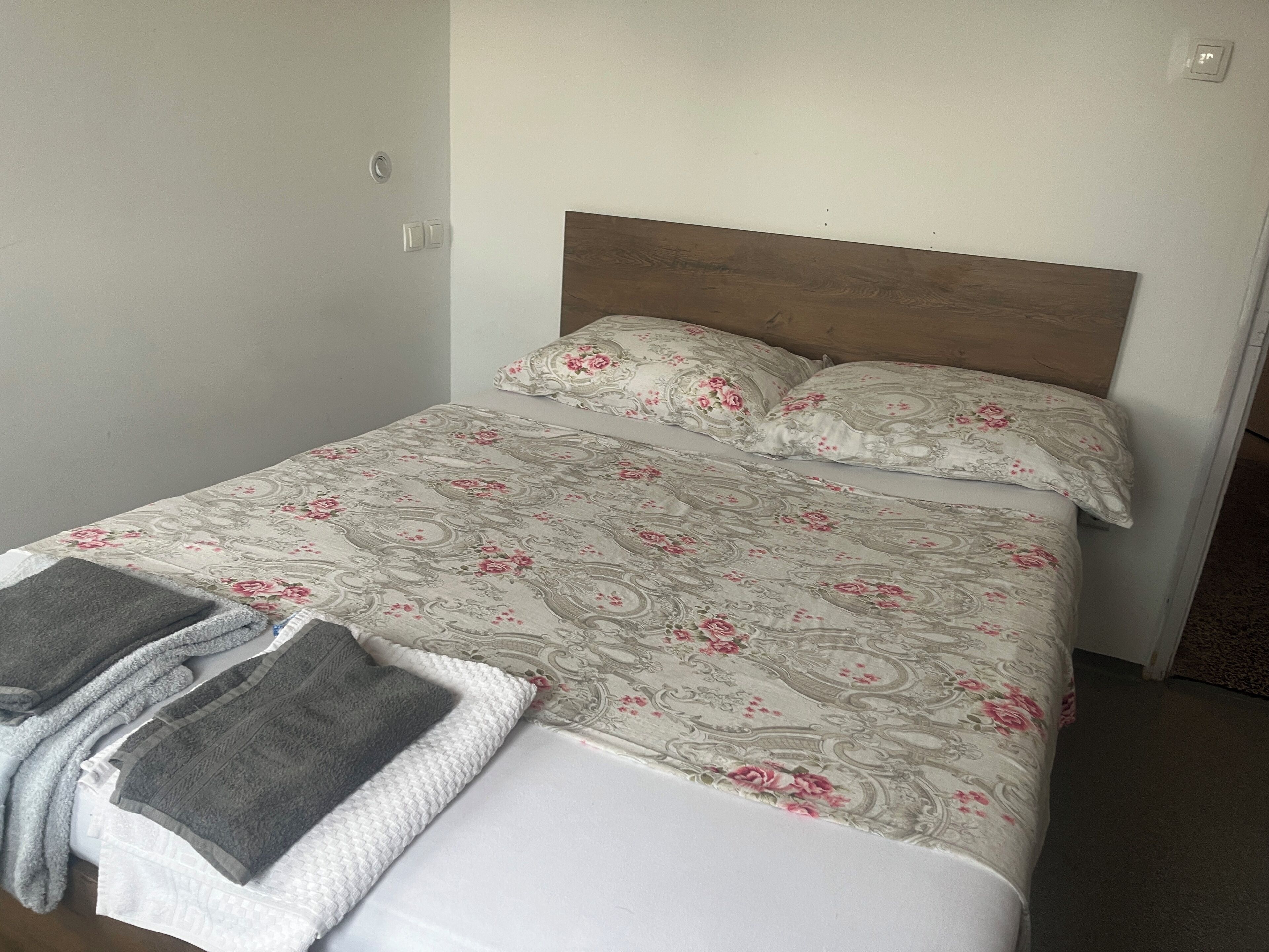 A neatly made bed with floral bedding, a wooden headboard, and two folded towels on the foot of the bed.