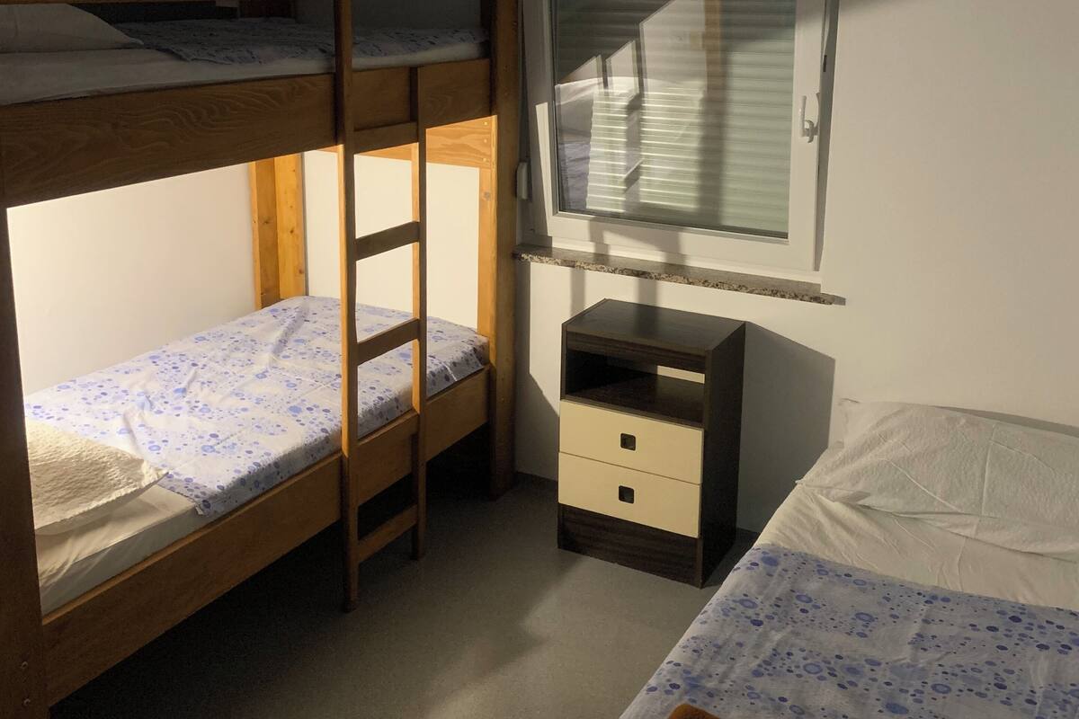 A dormitory room with bunk beds, a desk, and a window.