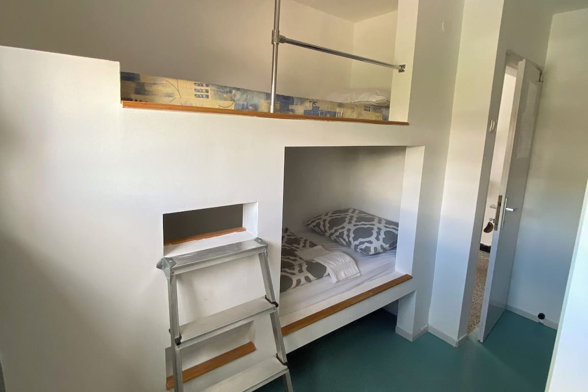 A dormitory room with bunk beds, a ladder, and a small table.