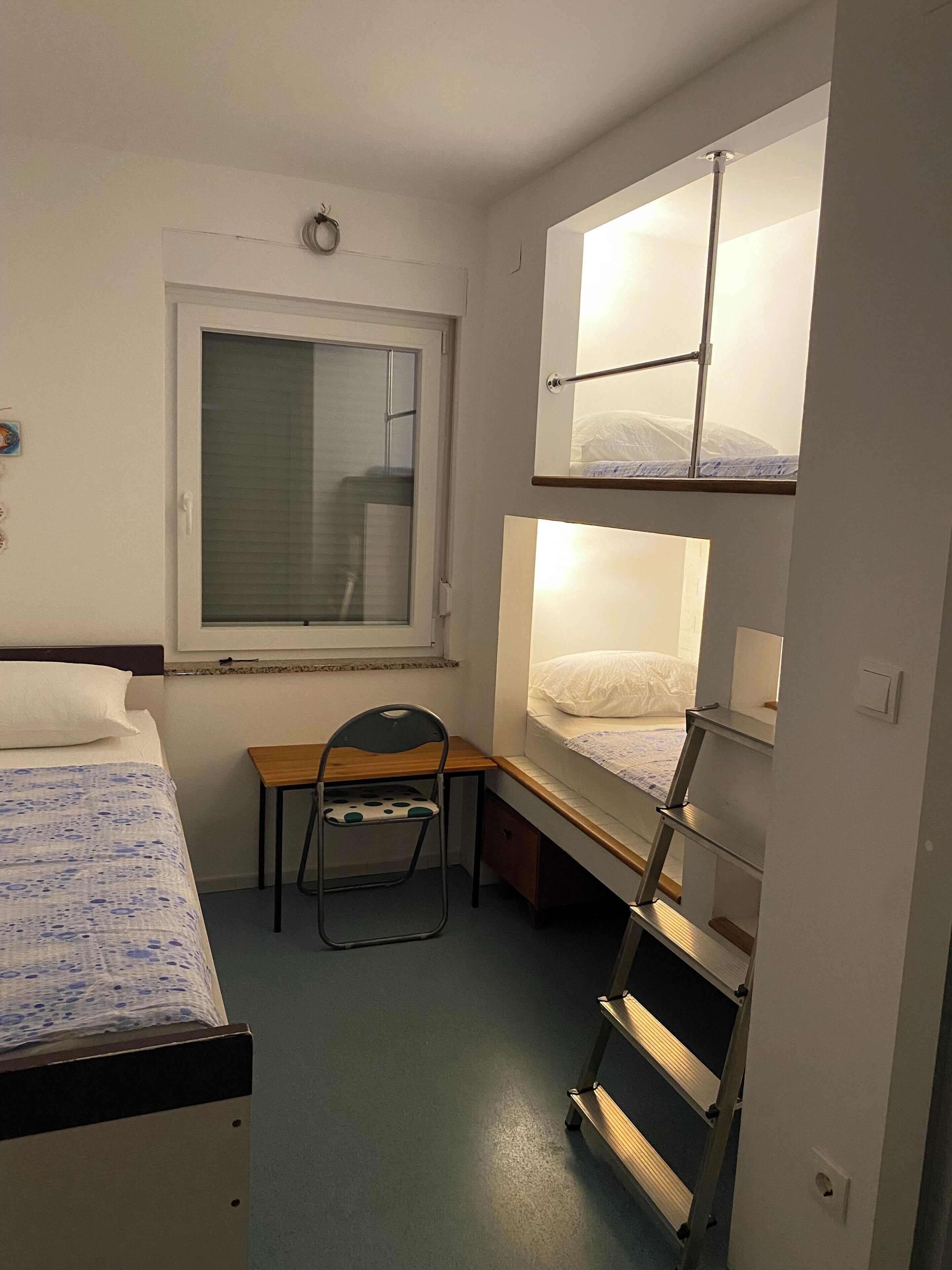 Un dormitorio con literas, un escritorio, una silla y una ventana.