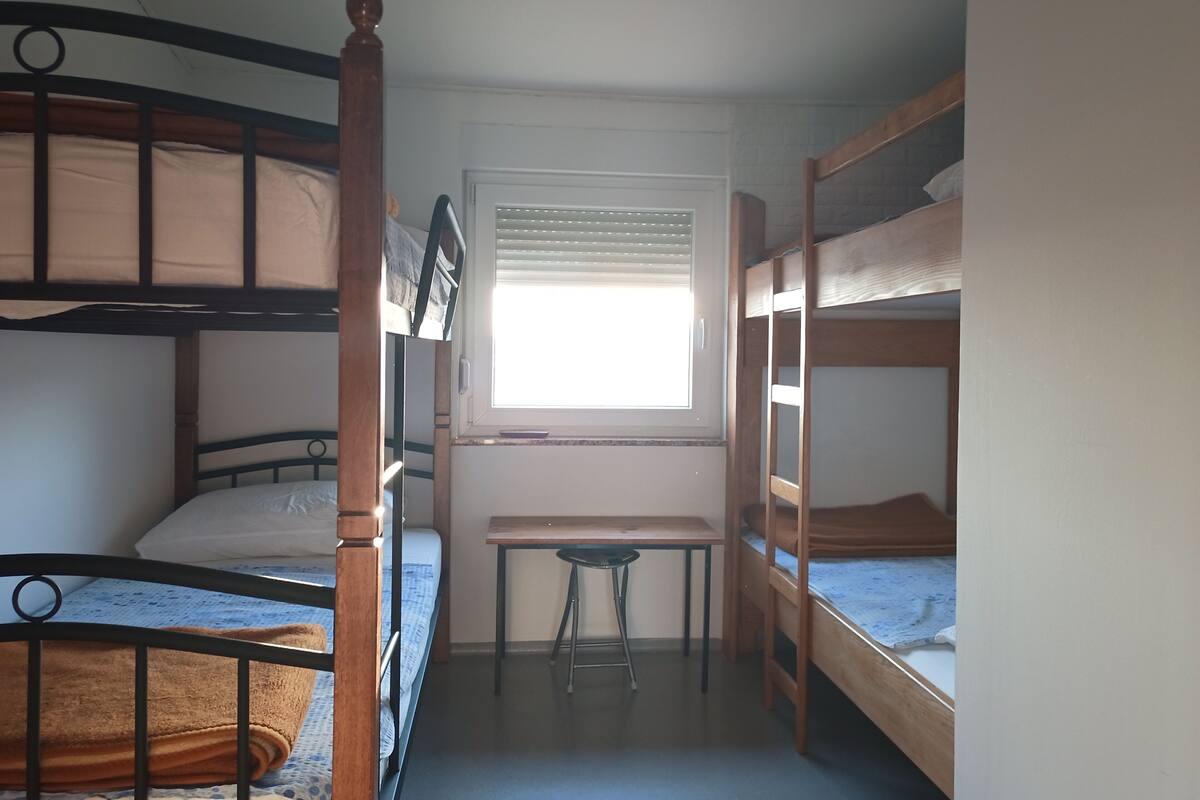 A dormitory room with bunk beds, a desk, and a window.
