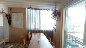 Een eetgedeelte met een lange houten tafel, stoelen en uitzicht door een glazen deur op een terras.