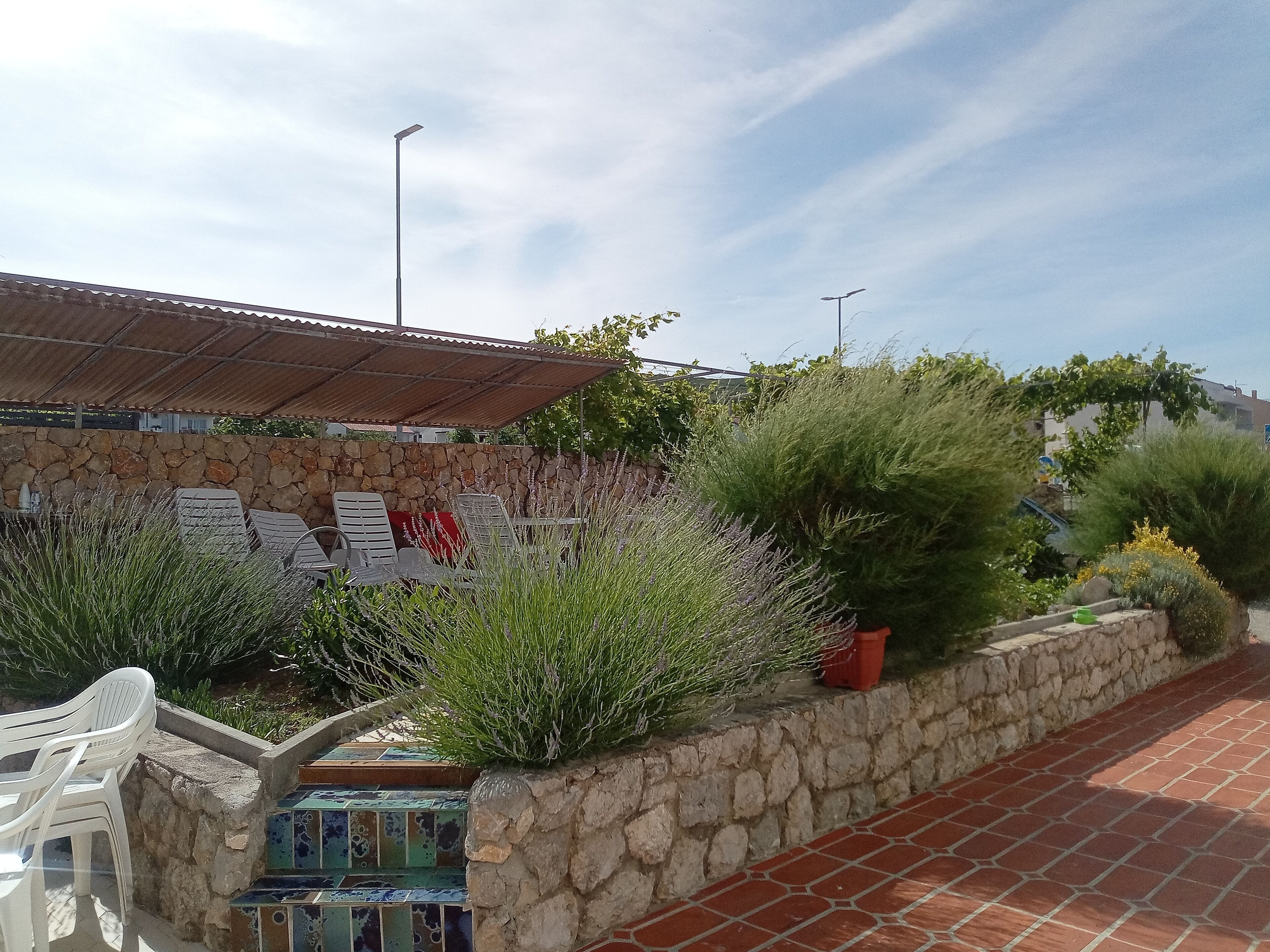 A stone wall with a tiled bench area, a metal roof, and a paved walkway.