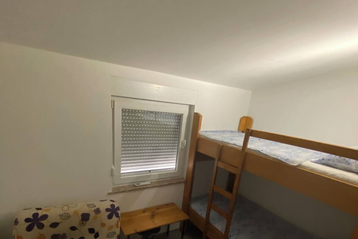 A small, cozy room with a bunk bed, a small table, and a cushioned chair.