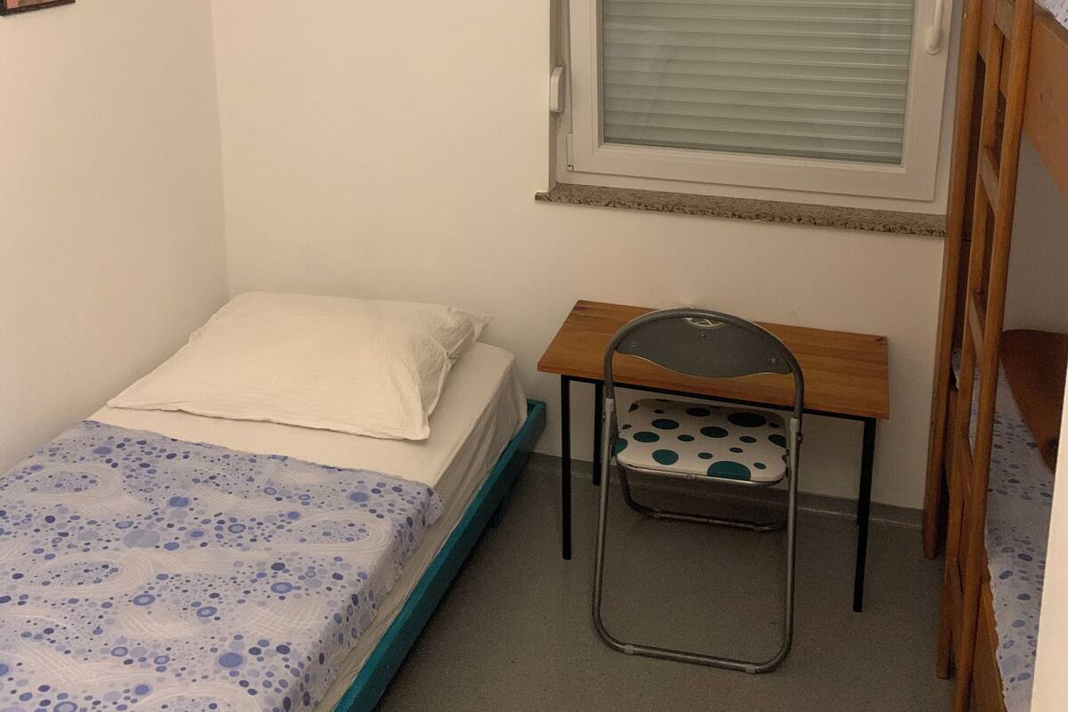 A small, single-bed room with a window, a desk, and a chair.