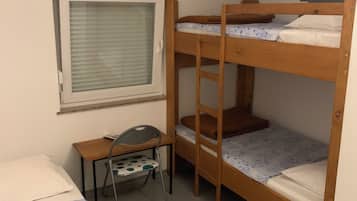 Habitación con literas, un escritorio y una silla, una ventana con persianas, y una cama con colcha estampada.
