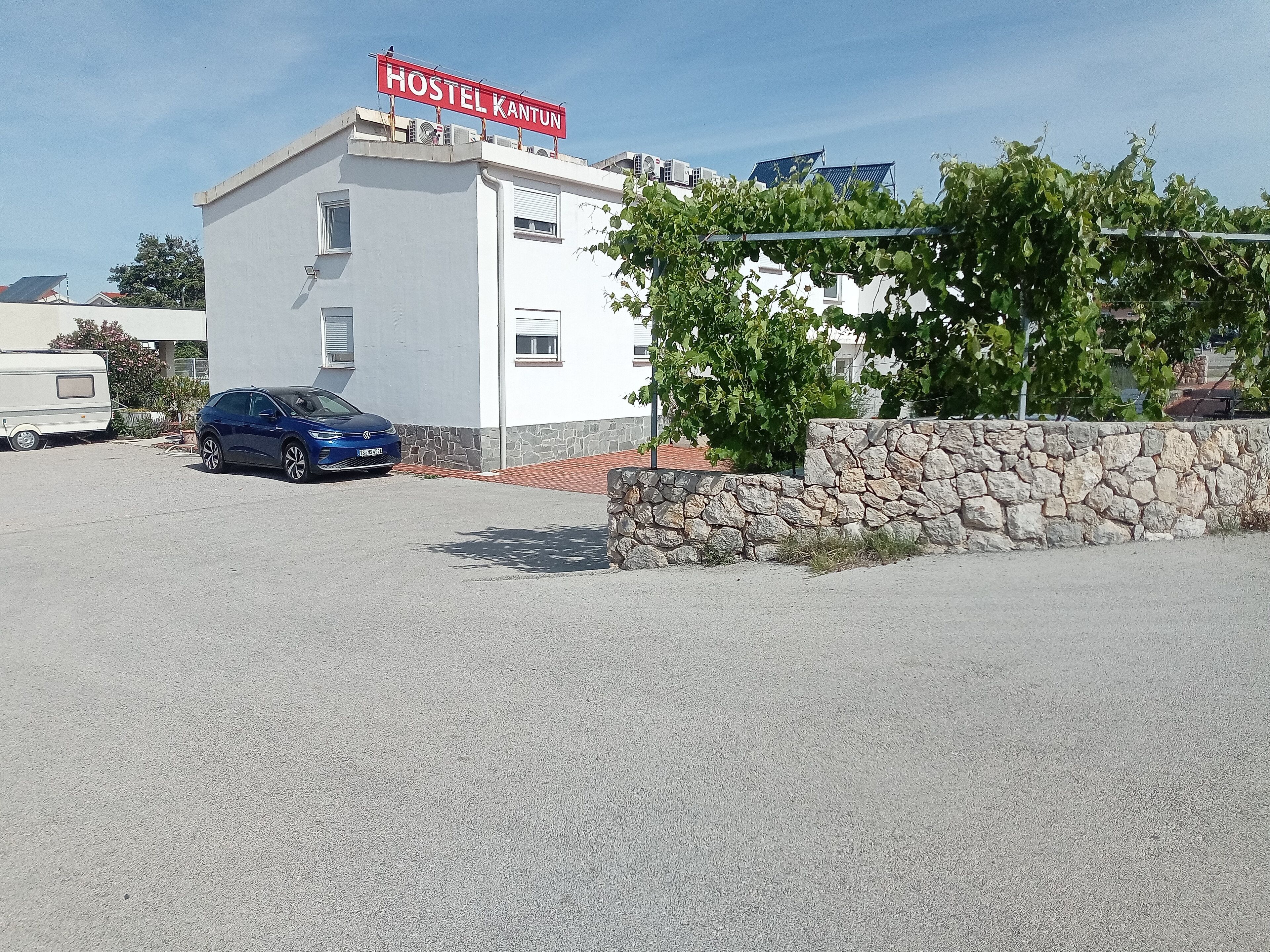 A building with a sign reading "HOSTEL KANTUN" and a stone wall in front.