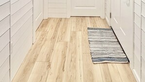 Un pasillo con paredes blancas, piso de madera, una puerta blanca y un espejo.