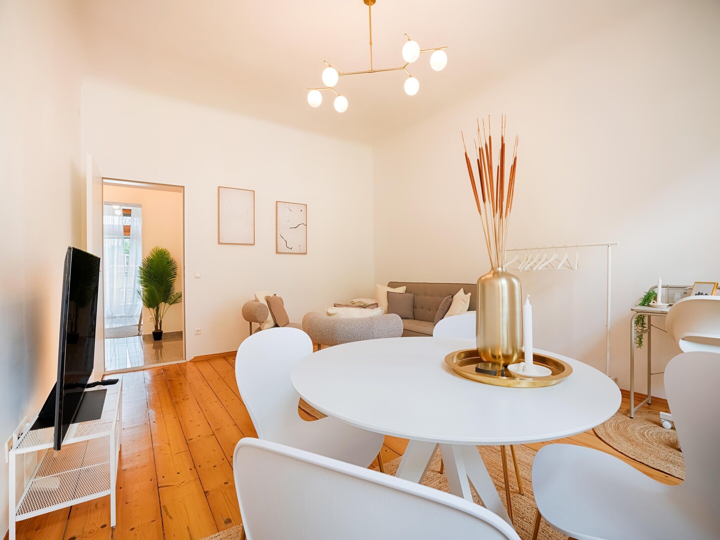 A modern living room with a round white table, white chairs, a sofa, a TV, and a decorative vase.