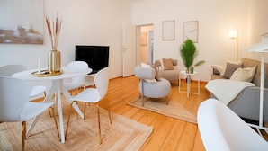 A modern living room with a white TV, a dining table with chairs, a sofa, and a coffee table. - Arcadio Home - Premium Suite (Graz)