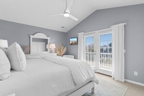 Ein Schlafzimmer mit Bett, Deckenventilator, Fernseher und einem Fenster mit VorhÀngen.