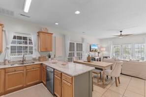 A modern kitchen with wooden cabinets, a built-in dishwasher, a dining area with a table and chairs, and a ceiling fan.
