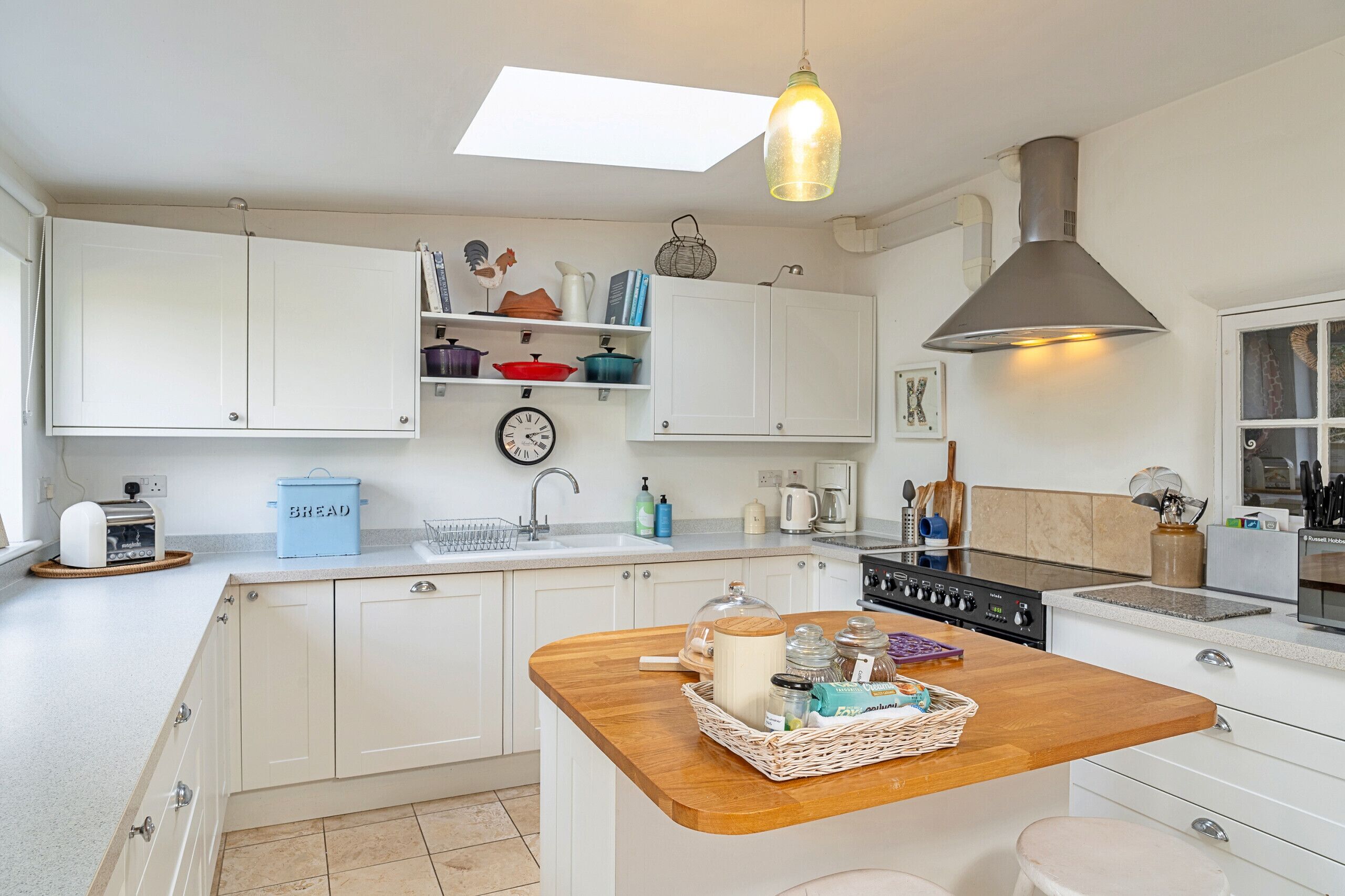Een moderne keuken met witte kasten, een centraal eiland met een houten aanrechtblad, een inbouwfornuis en een dakraam.