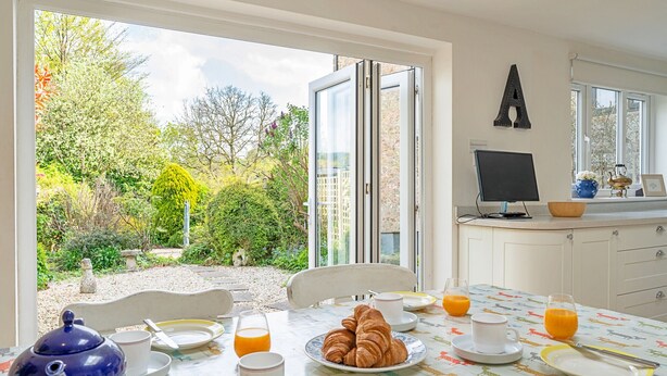Una tavola per la colazione apparecchiata con croissant, succo d'arancia e tè, con vista su un giardino alberato e un edificio sullo sfondo.