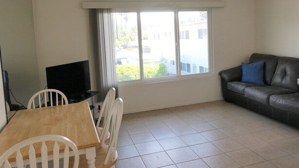Ein Wohnzimmer mit Esstisch, Stühlen, einer Couch, einem Fernseher und einem Fenster mit Vorhängen.