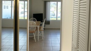 Ein Zimmer mit Esstisch und Stühlen, einem Fernseher und Blick durch große Fenster nach draußen.