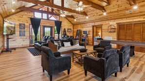 A spacious wooden cabin interior with a large sofa, multiple armchairs, a pool table, and ceiling fans. - Splash Mountain Lodge 8 Bedroom Cabin (Sevierville)