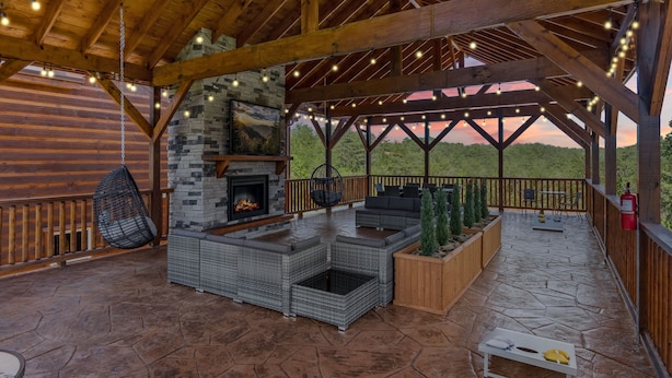 A covered outdoor patio with a stone fireplace, wicker furniture, and string lights. - Splash Mountain Lodge 8 Bedroom Cabin (Sevierville)