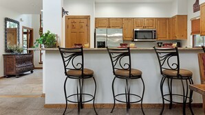 Een moderne keuken met houten kastjes, een roestvrijstalen koelkast en drie barkrukken met beklede zitplaatsen.