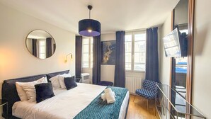 A hotel room with a large bed, a round mirror, a TV, and a window with curtains.