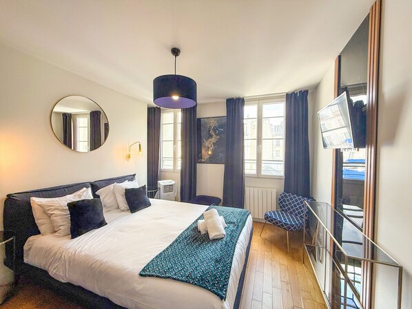 Habitación de hotel con una cama grande, un espejo redondo, un televisor y una ventana con cortinas.