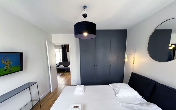 Una habitación de hotel moderna con una cama grande, un armario, un espejo y un televisor en la pared.