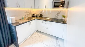 A modern kitchen with white cabinets, a stainless steel range hood, and a marble backsplash.