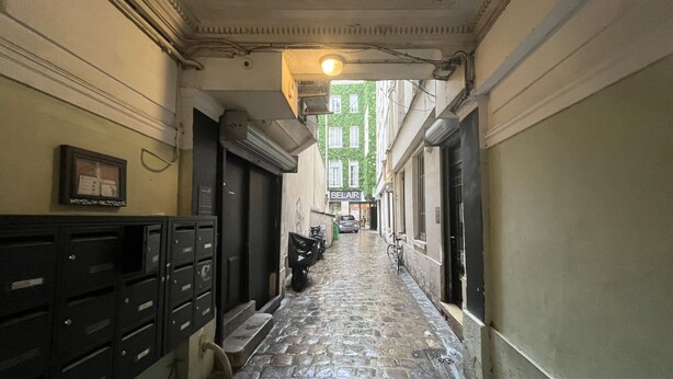 A narrow alleyway with a cobblestone path, a bicycle, and a car parked in the distance.